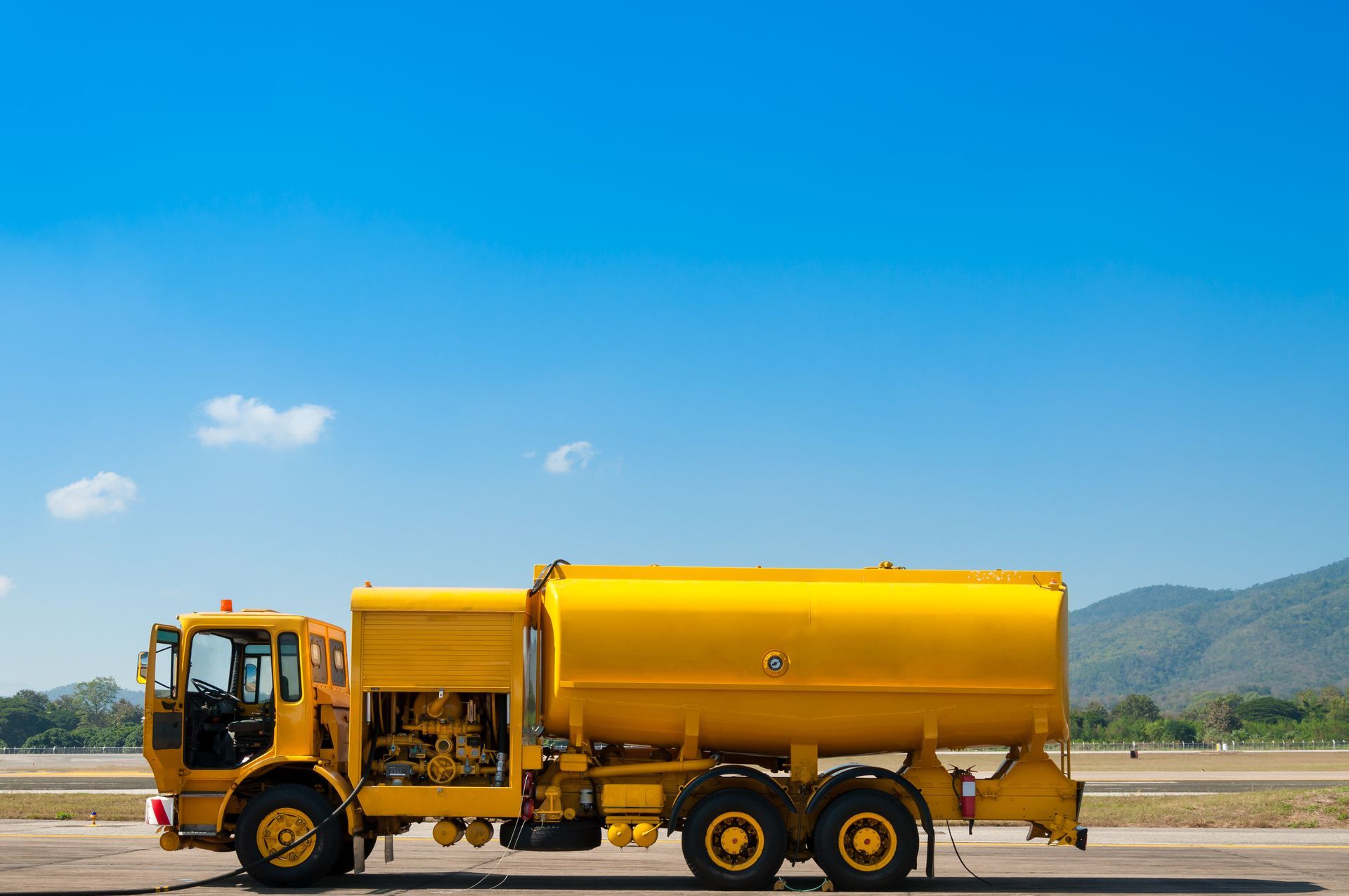 Yellow street sweeper truck parked on a road with mountains and blue sky in the background