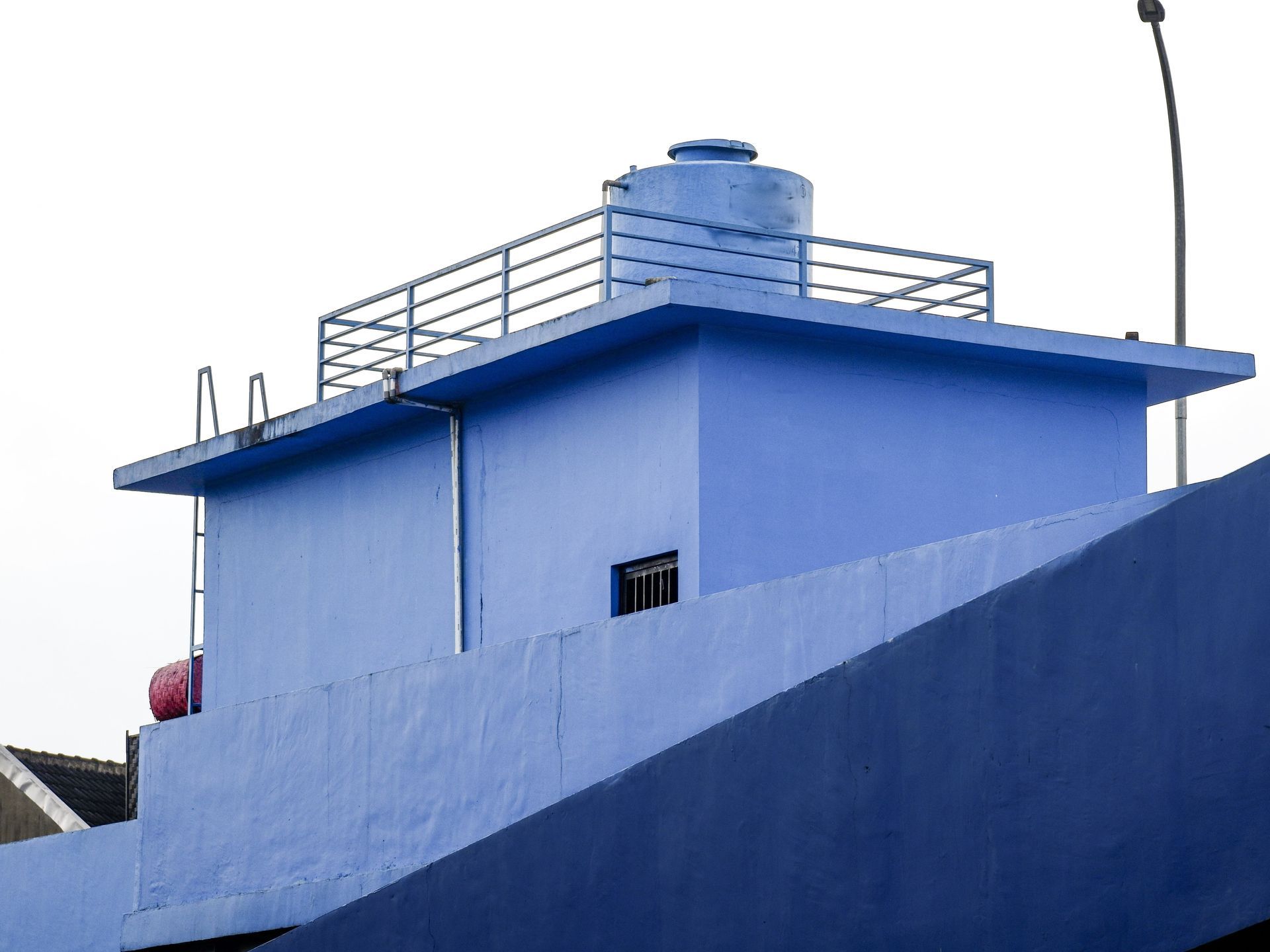 Blue building with rooftop railing and water tank, viewed from below against the sky