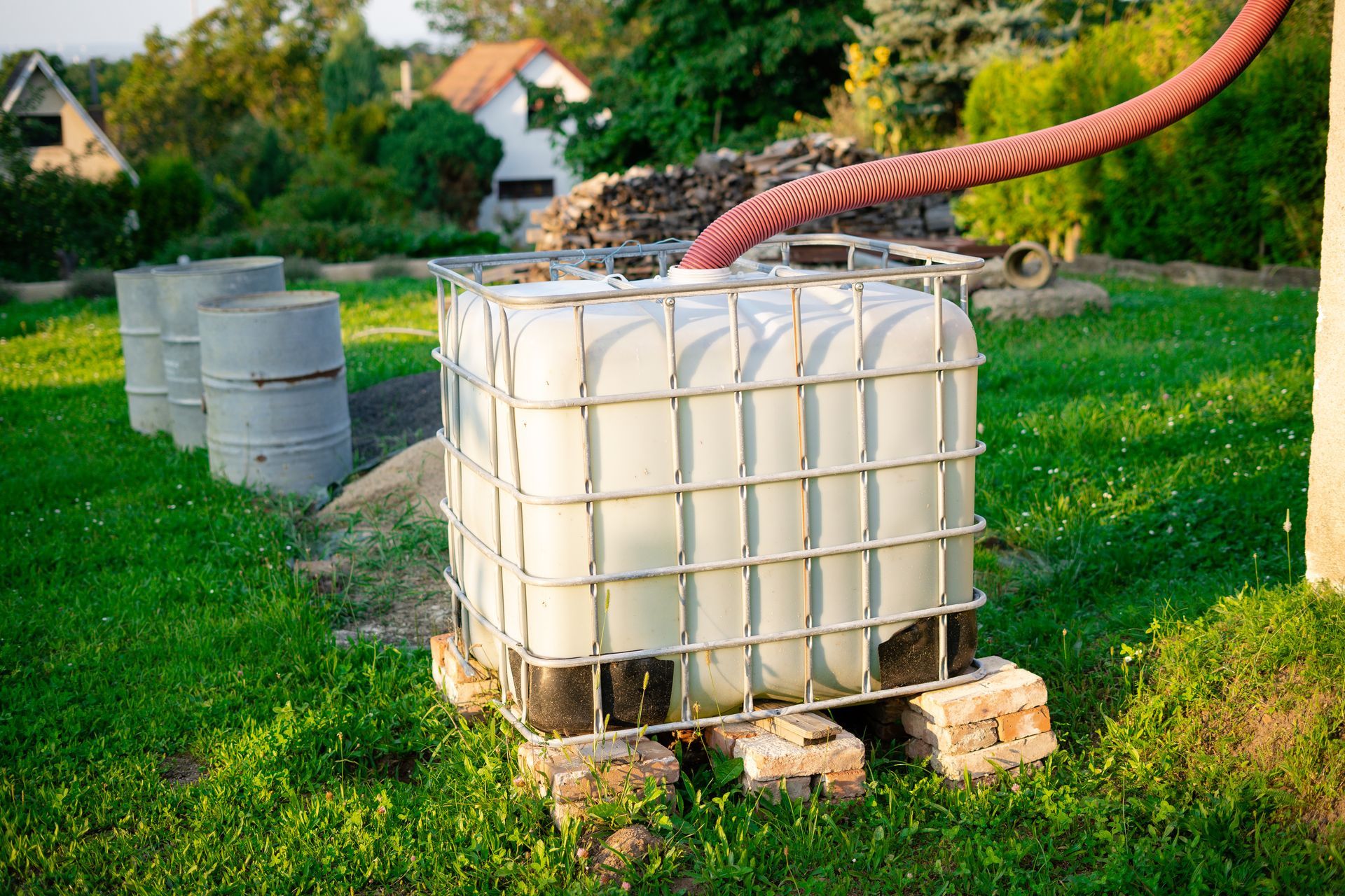 Large white water tank on pallets in a grassy yard, with a hose attached and concrete blocks nearby