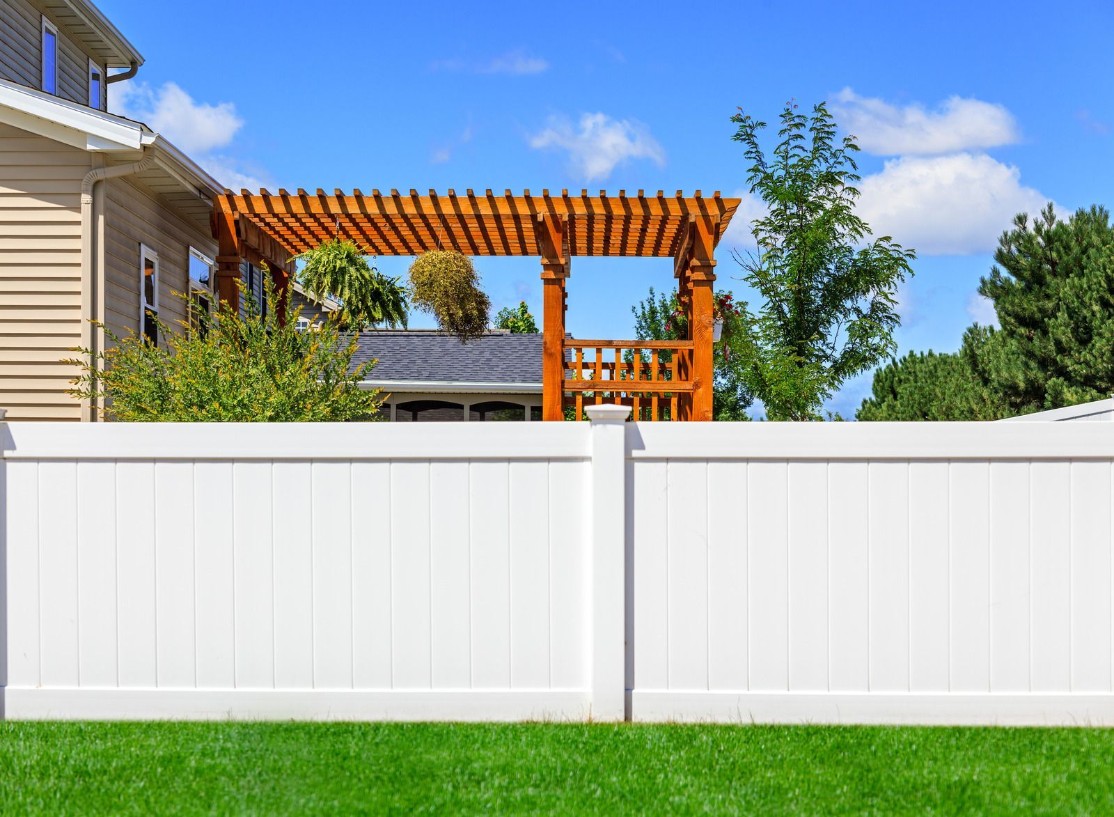A white fence with a wooden pergola in the backyard of a house.