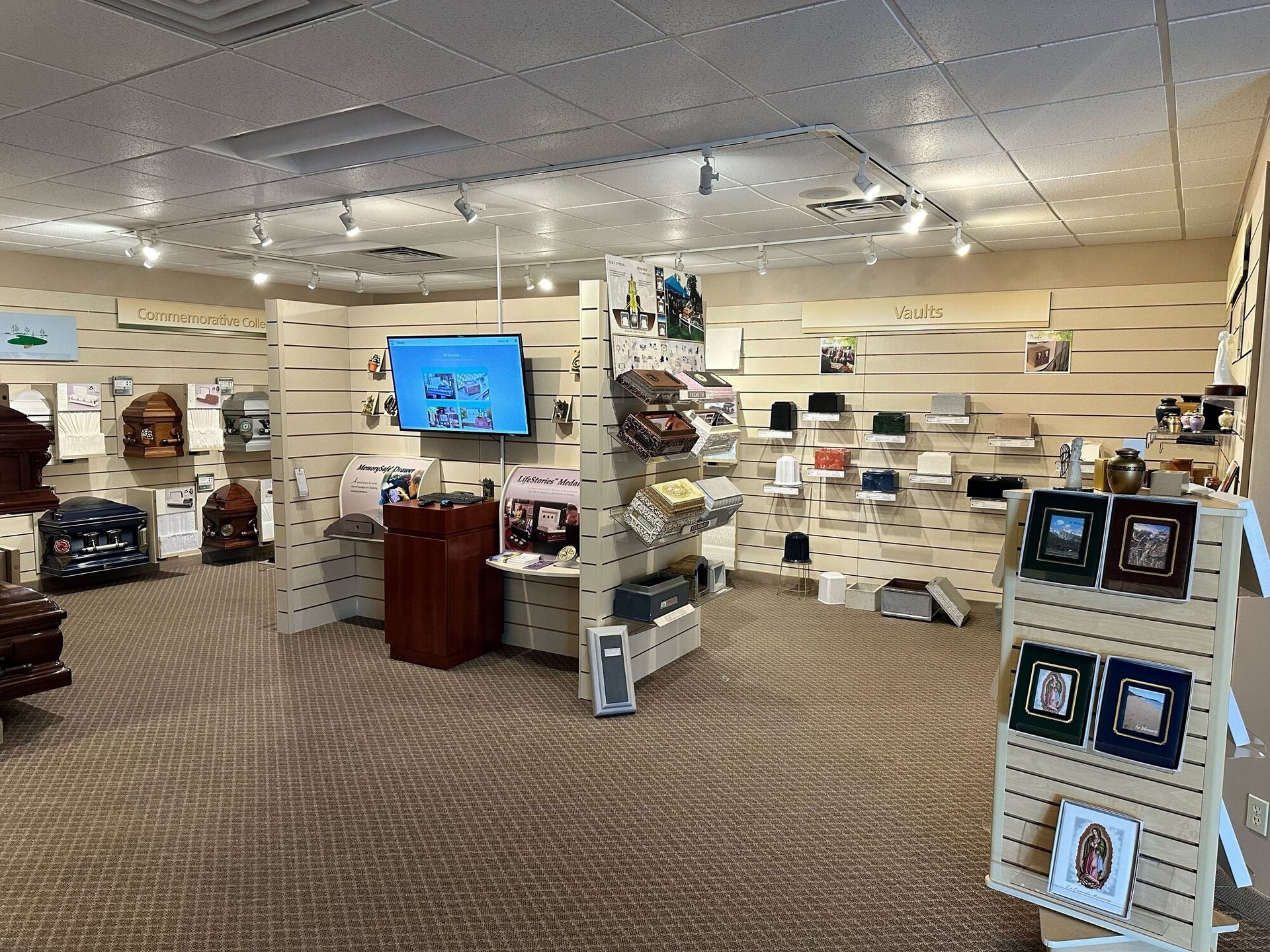 Interior of a gift shop with displays of various items, beige walls and carpet, with a TV screen on.