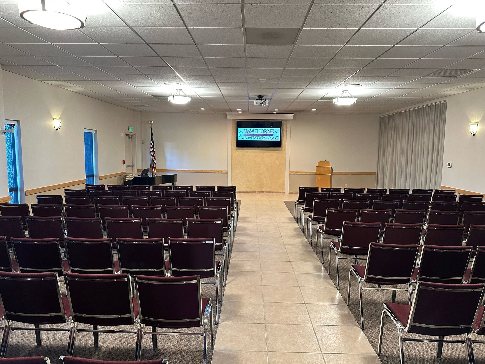 Rows of chairs face a stage in a beige room with a screen and podium.