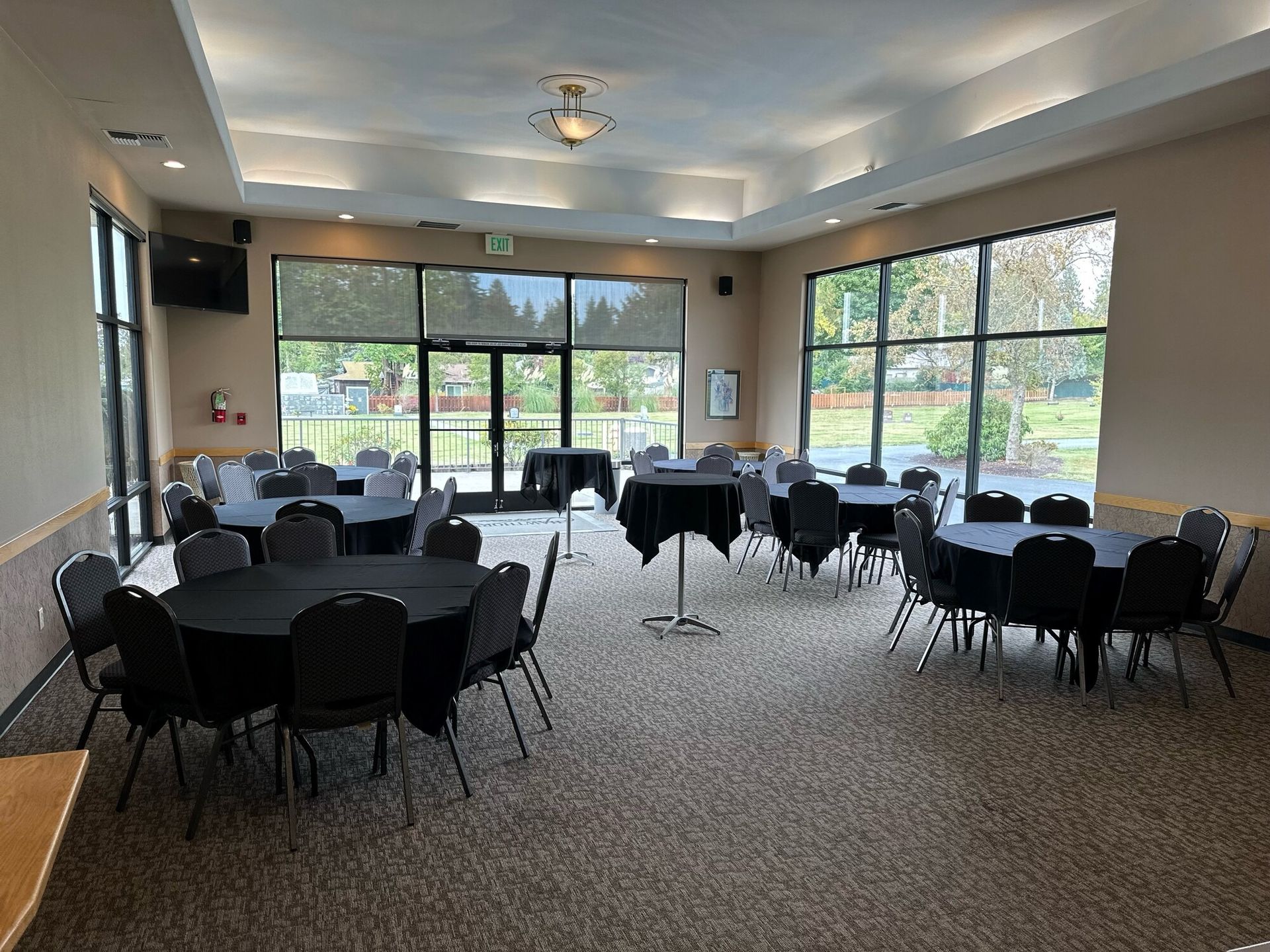 Event room with round tables draped in black, set for guests. Windows offer outdoor views.