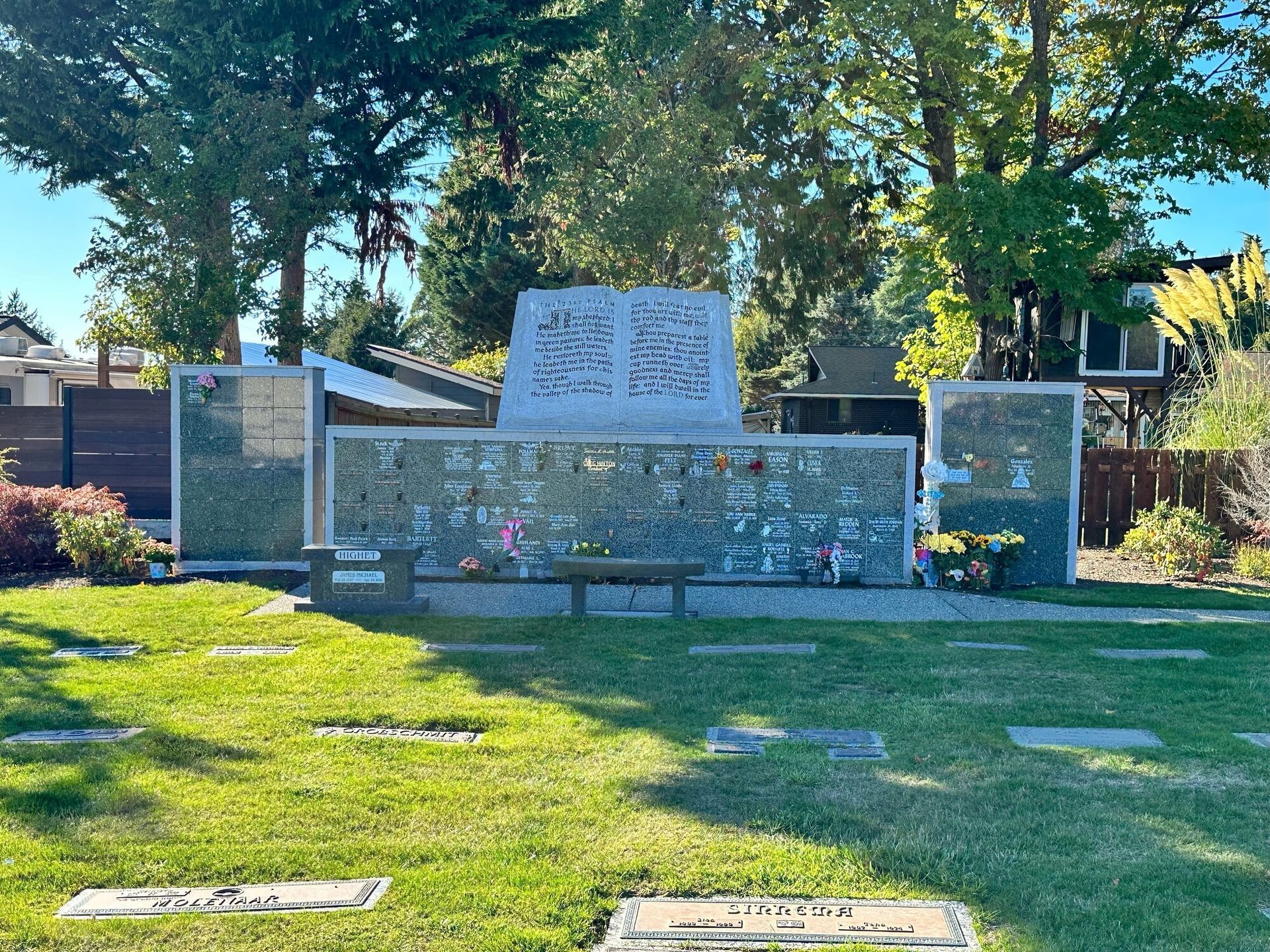 Memorial with a central stone structure and niches for cremains; green grass and trees surround.