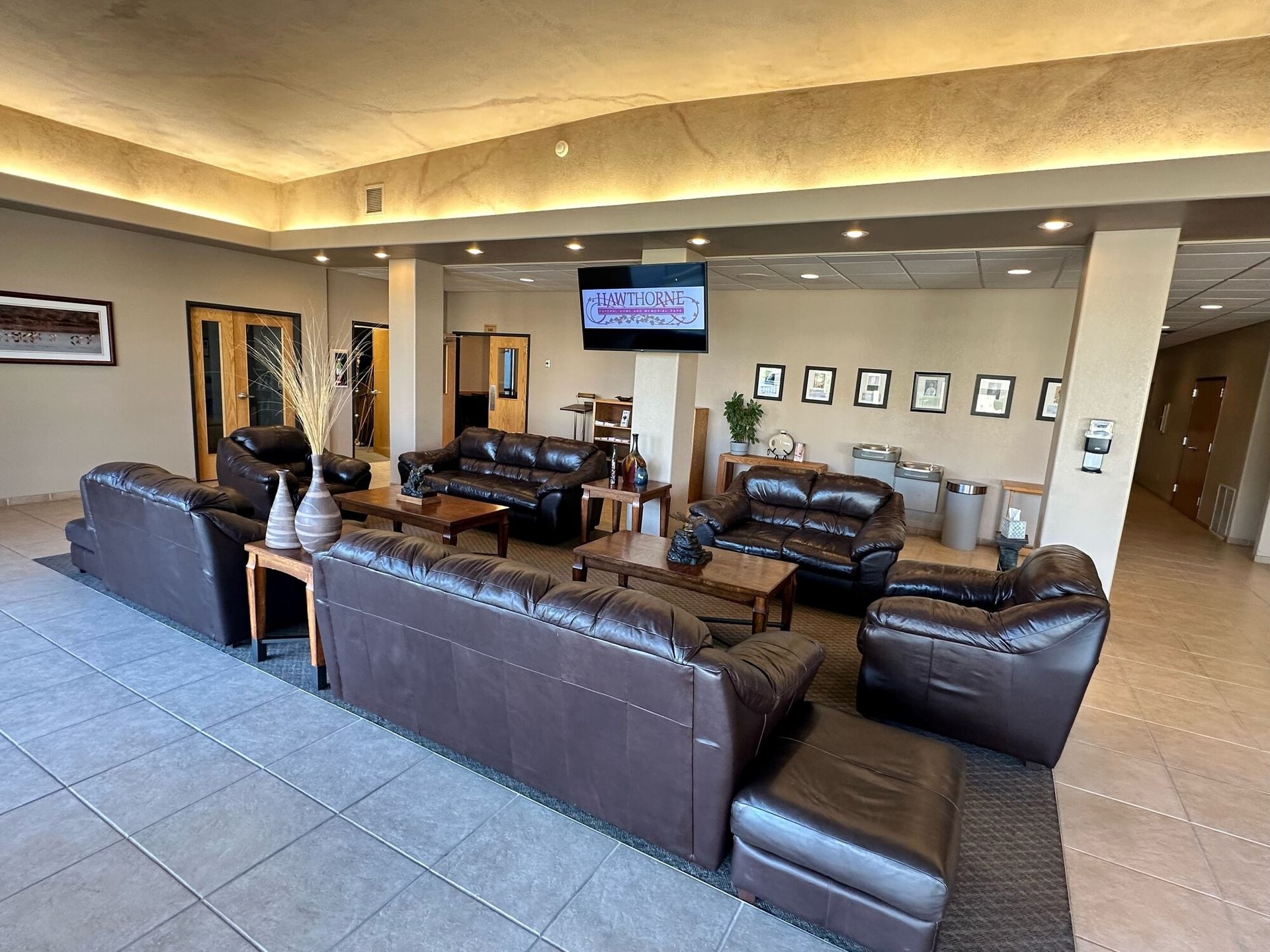 Lounge area with brown leather couches, tables, and a TV; neutral-toned walls and flooring.