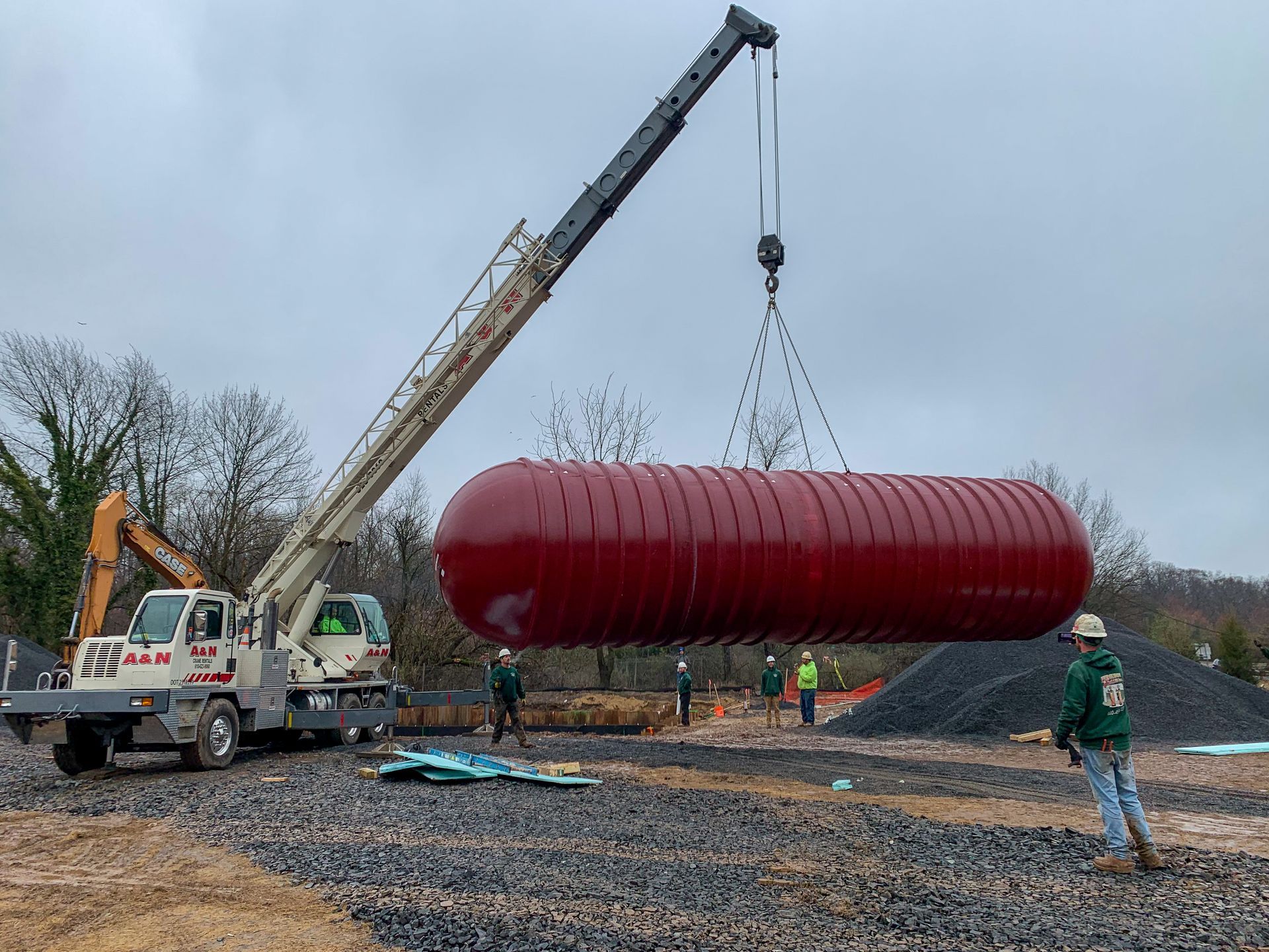 A large red tank is being lifted by a crane from A&N Crane Rental.
