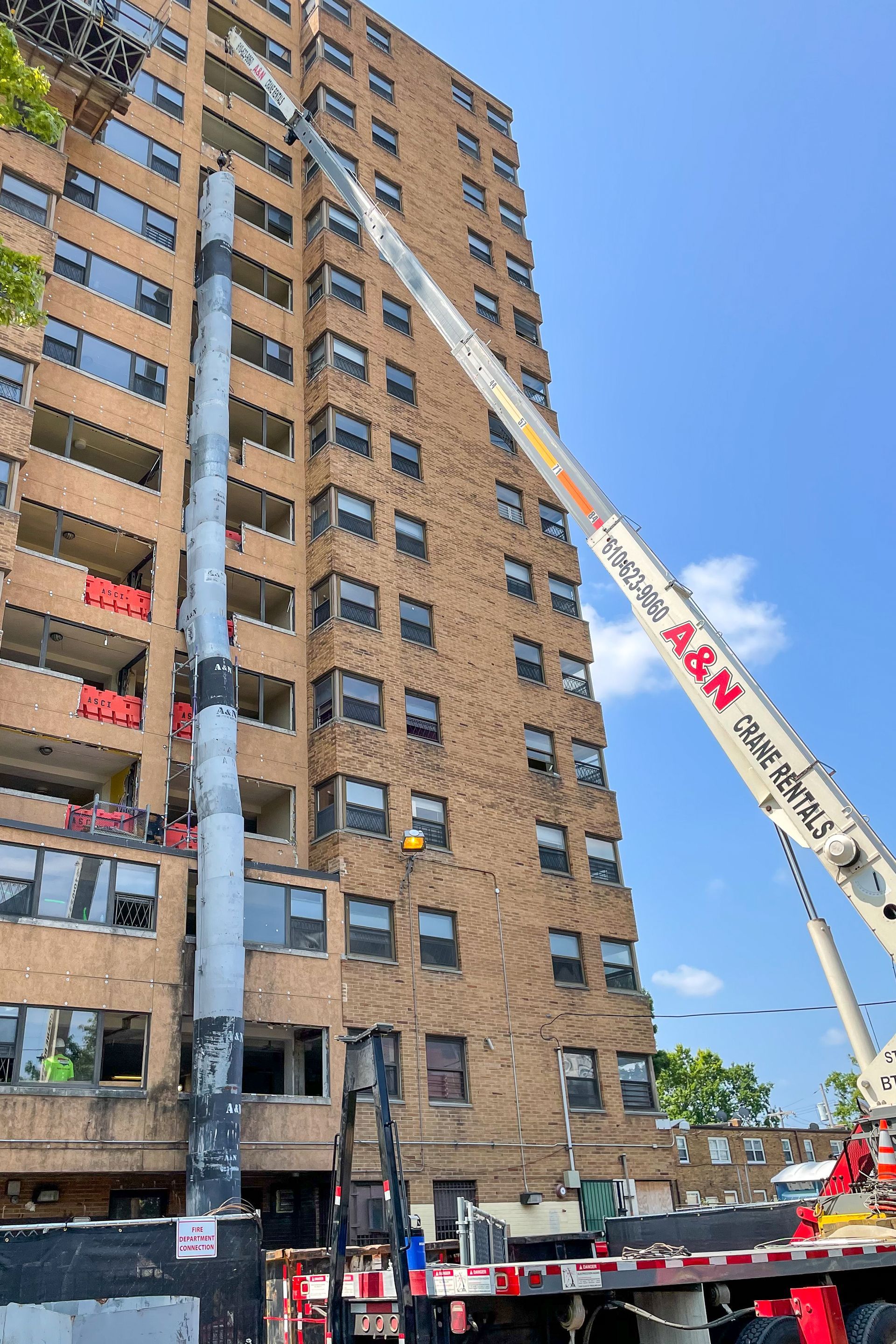 A large brick building with a crane on top of it. The crane from A&N Crane Rental is installing a metal trash chute. 