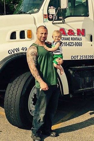Nick Crocetto Jr. is holding his son in front of an A&N Crane Rental crane. 