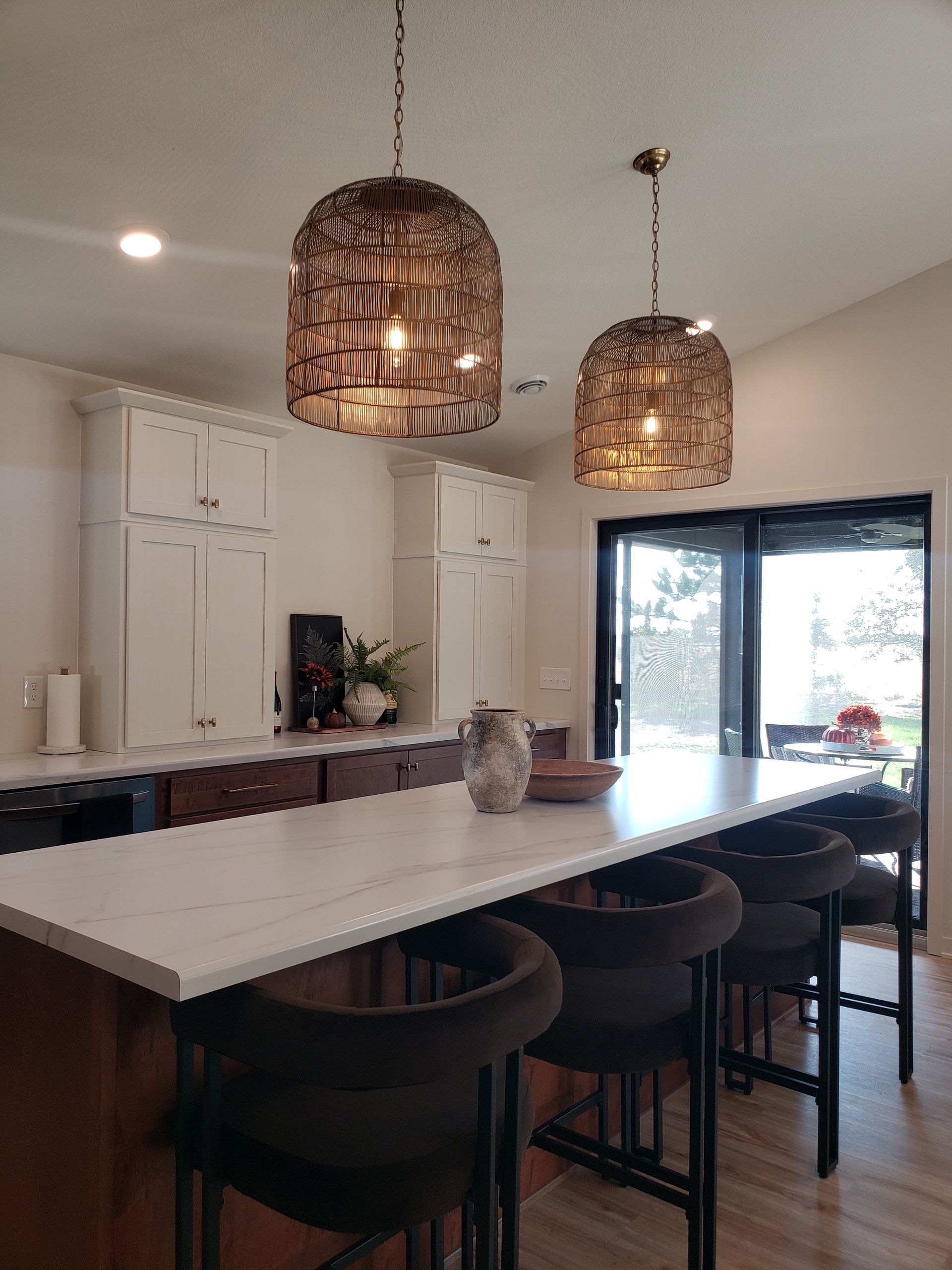 Kitchen with island, pendant lights, white countertops, dark brown bar stools, and cabinets.