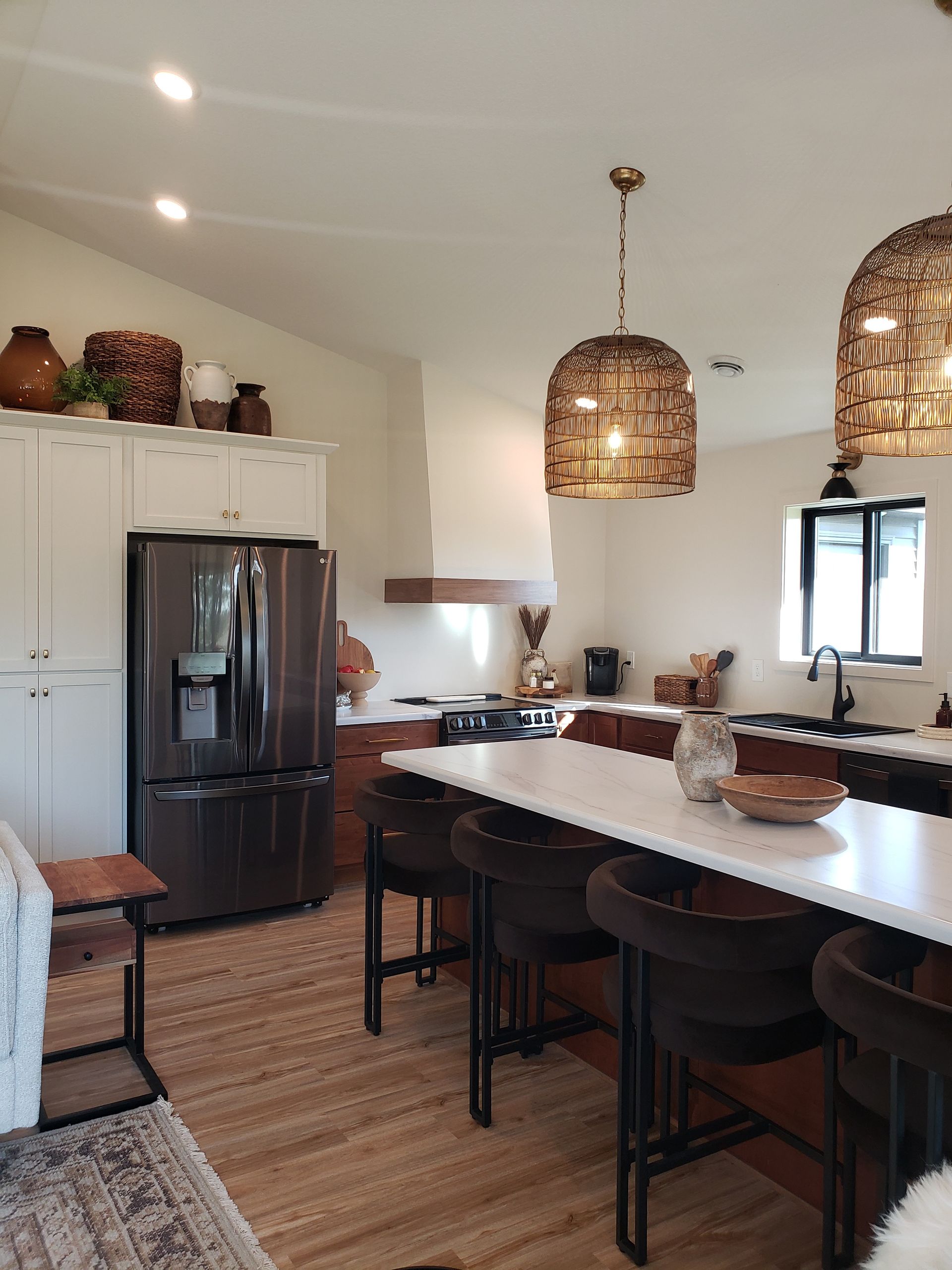 Modern kitchen with white cabinets, brown island, black fridge, and woven pendant lights.