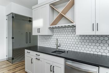 A kitchen with white cabinets , black counter tops , and a wine rack.