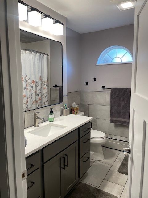 Bathroom with gray vanity, white sink, toilet, and floral shower curtain. Pale purple walls.