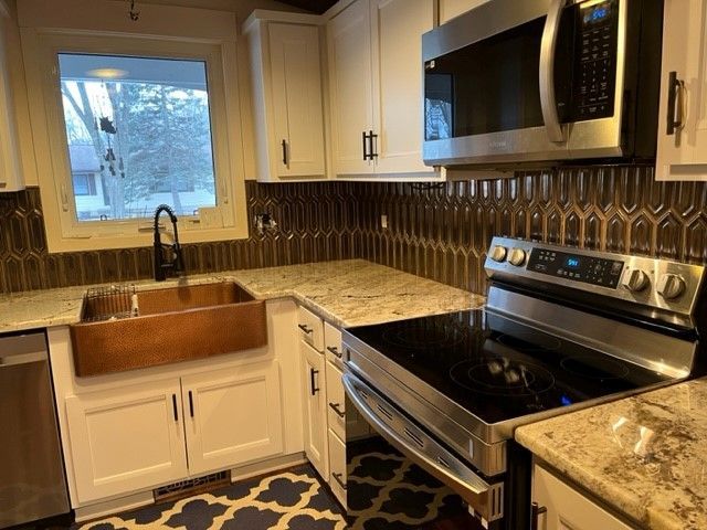 White kitchen with copper sink, granite counters, and brown tile backsplash.