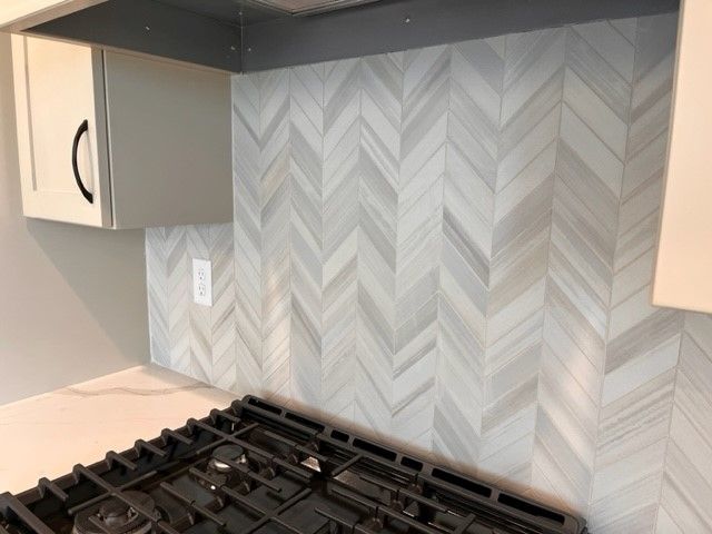 A kitchen with a stove top oven and a herringbone tile wall.