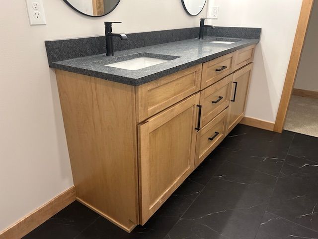Light wood double bathroom vanity with black countertop and hardware.