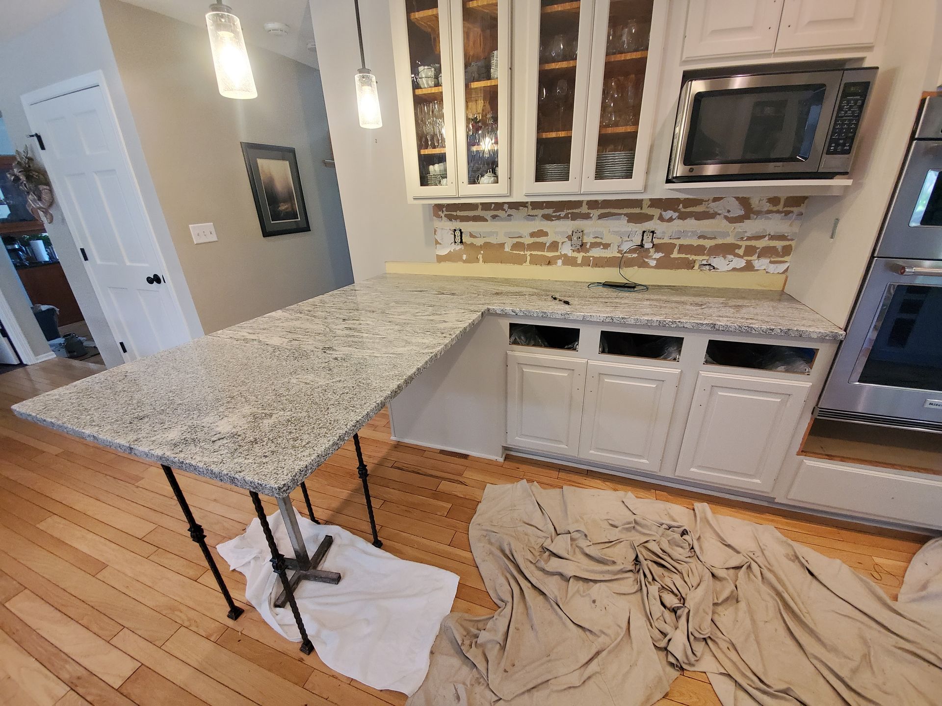 Kitchen renovation: granite countertop on temporary supports, unfinished cabinets, oven, and microwave.