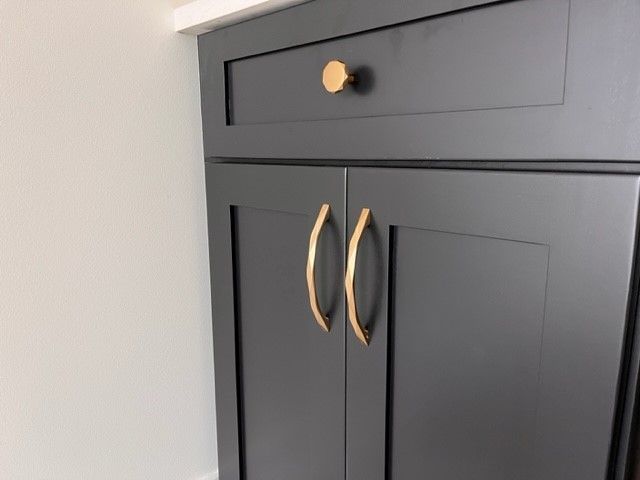 A black cabinet with gold handles and a drawer