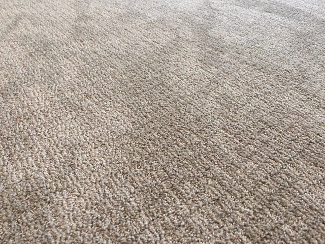 A close up of a beige rug on a carpeted floor.