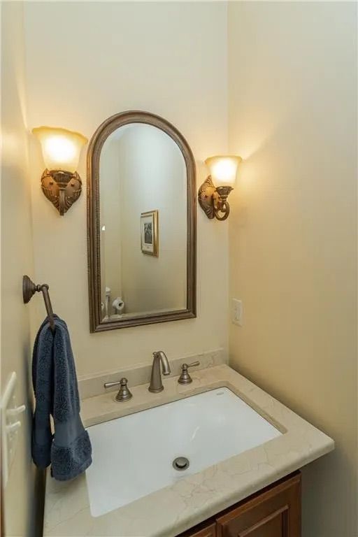Small bathroom with a sink, mirror, sconces, and towel. Beige walls, white sink, brown vanity.