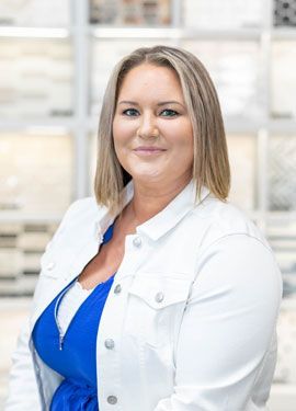 A woman wearing a white jacket and a blue top is smiling for the camera.