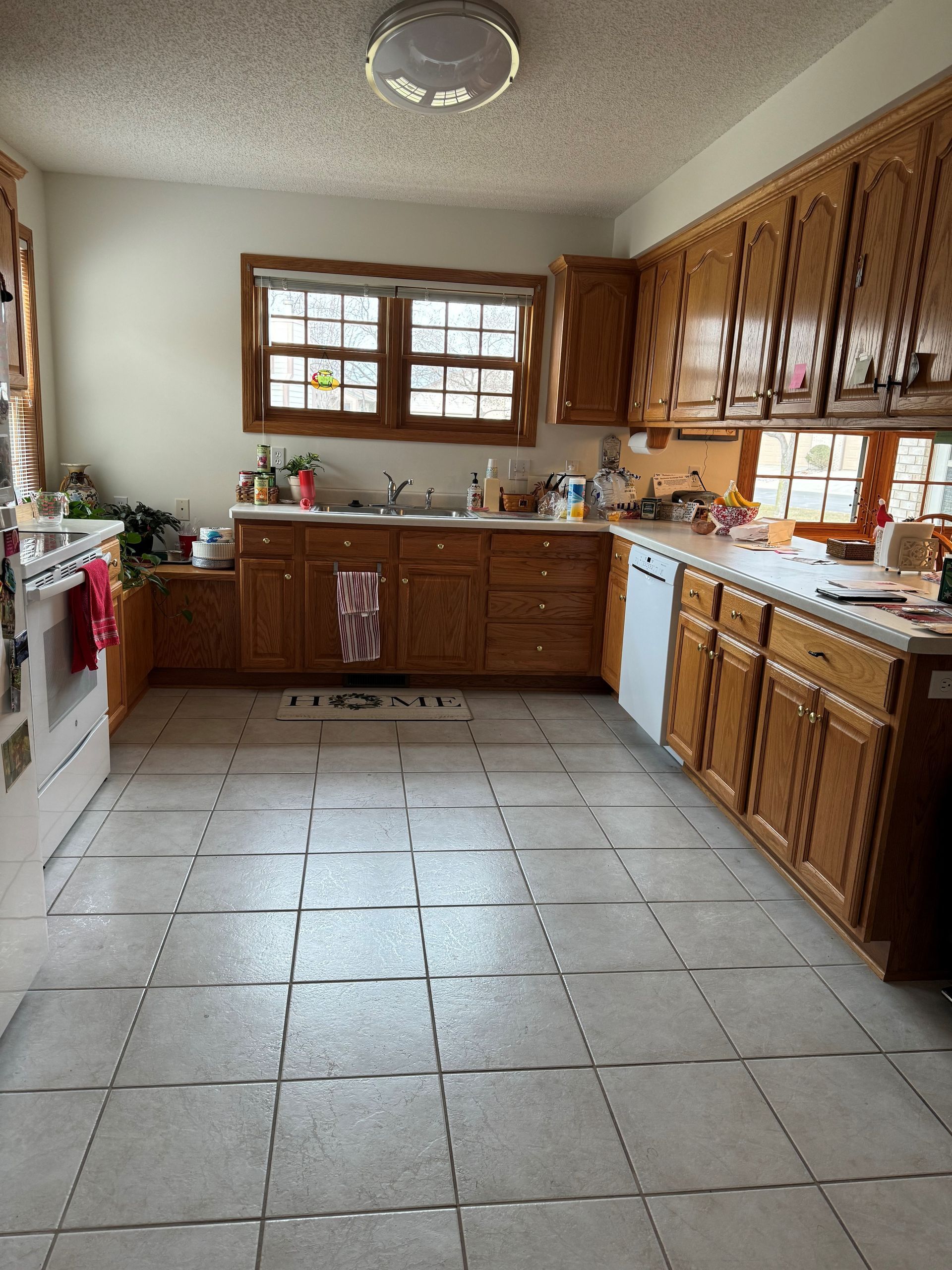 Kitchen with wood cabinets, white appliances, and tile floor. Window over the sink and fluorescent light.