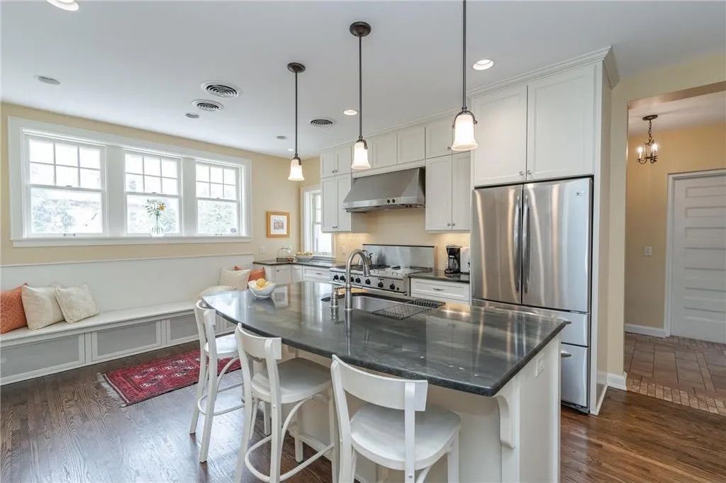 Kitchen with white cabinets, stainless steel appliances, island with stools, and window seat.
