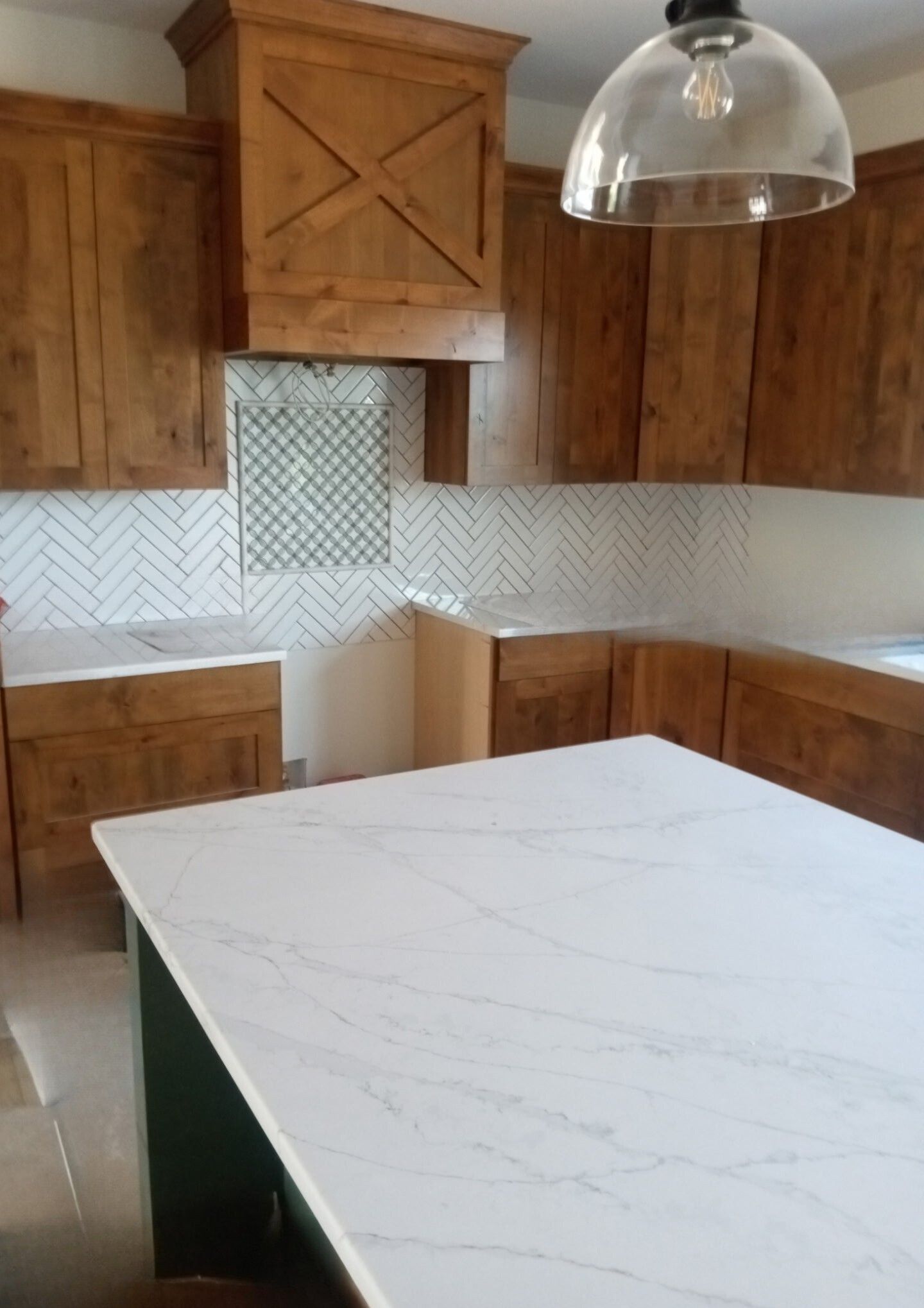 Kitchen with light countertops, wooden cabinets, white and gray backsplash, and a kitchen island.