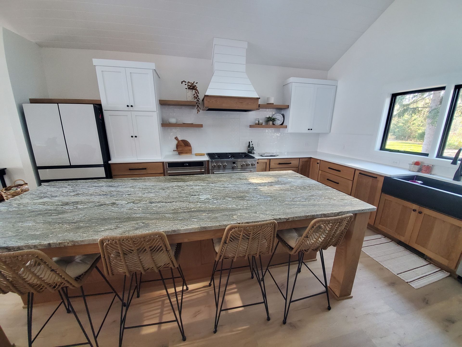 Modern kitchen with large island, wood cabinets, granite countertop, and woven bar stools.