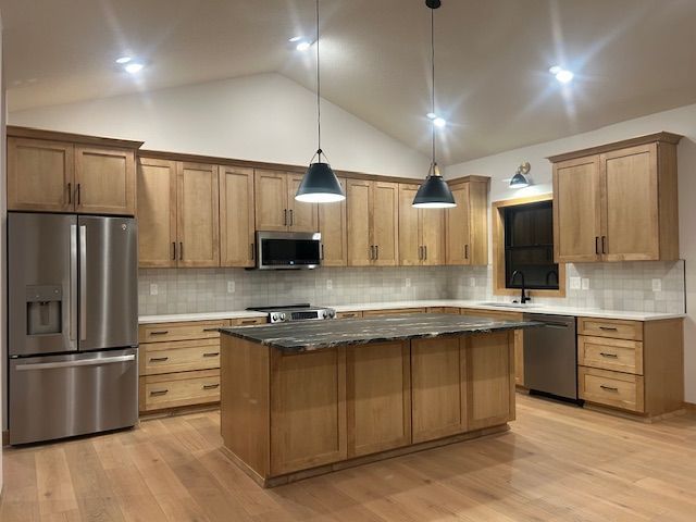 Modern kitchen with light wood cabinets, island, stainless steel appliances, and pendant lights.