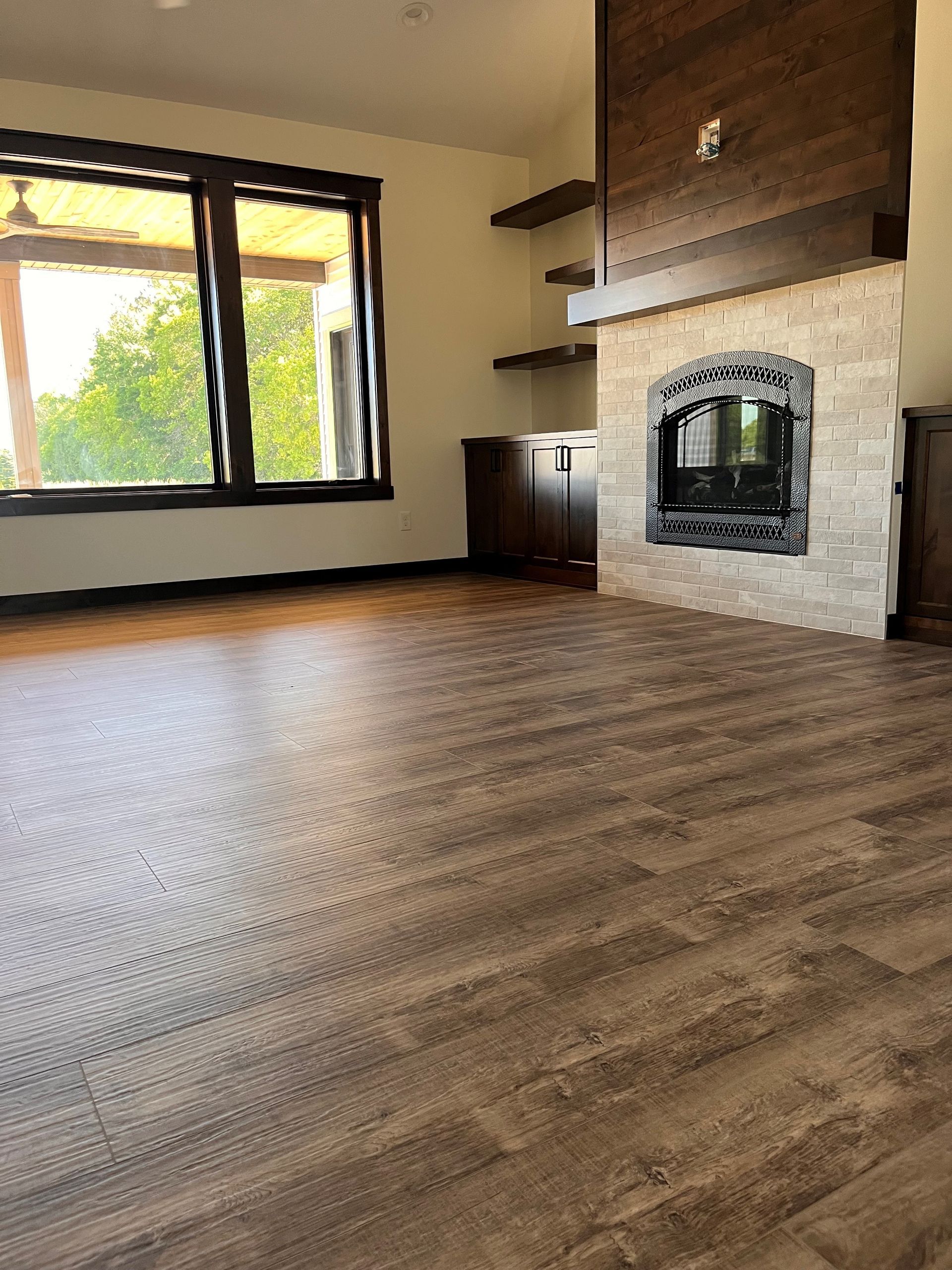 Spacious room with wood-look flooring, fireplace, large window, and neutral walls.