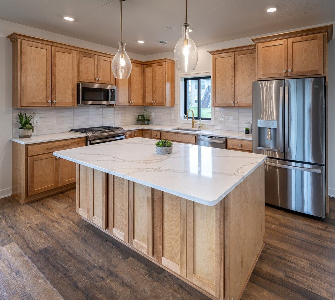 A modern kitchen with light wood cabinets, white countertops, and stainless steel appliances.