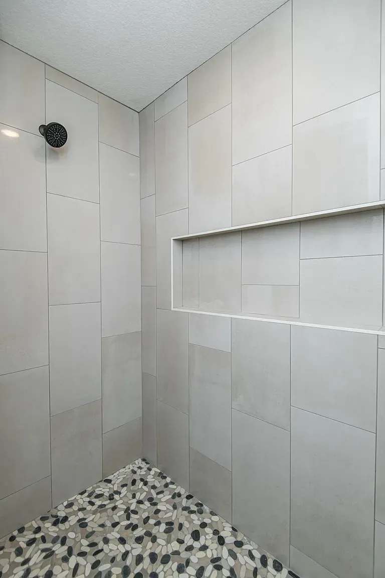 Gray-tiled shower with pebble floor, built-in shelf, and black showerhead.