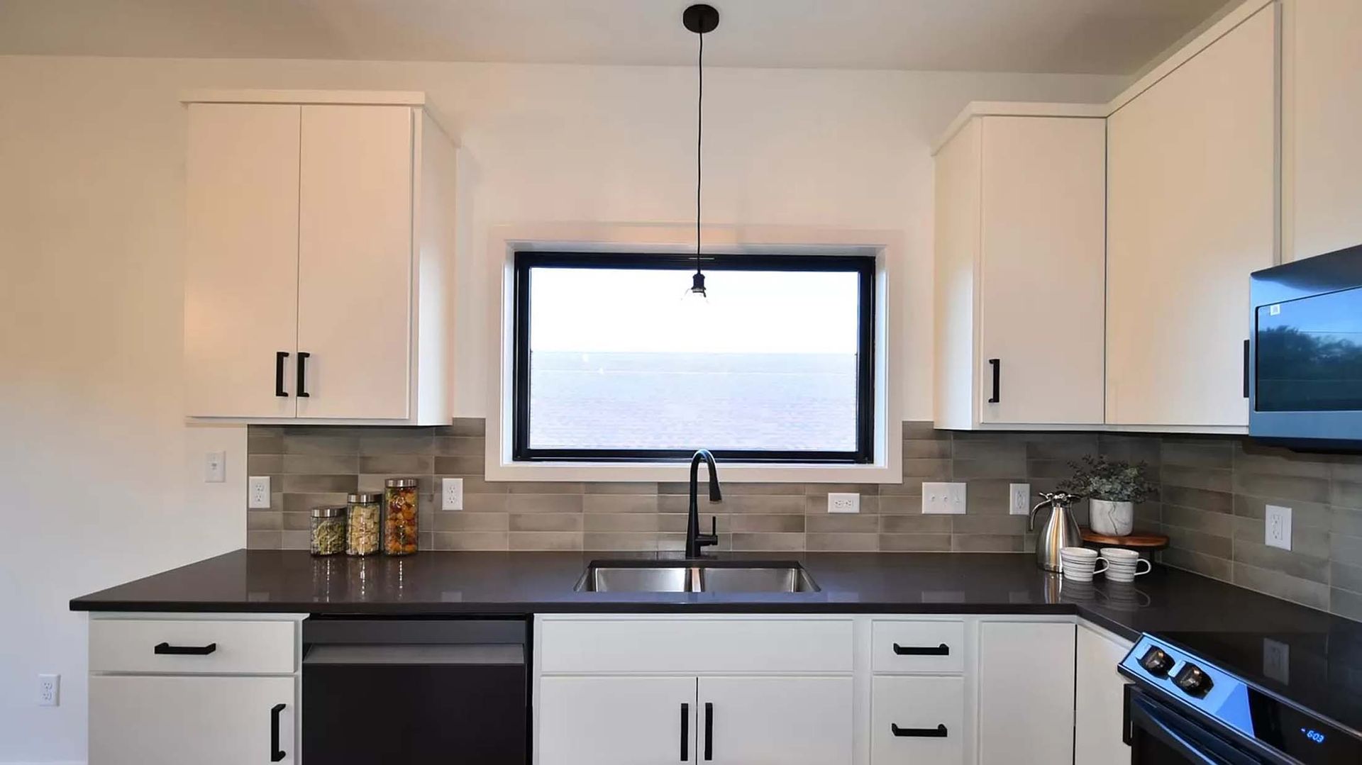 A kitchen with white cabinets , black counter tops , a sink and a window.