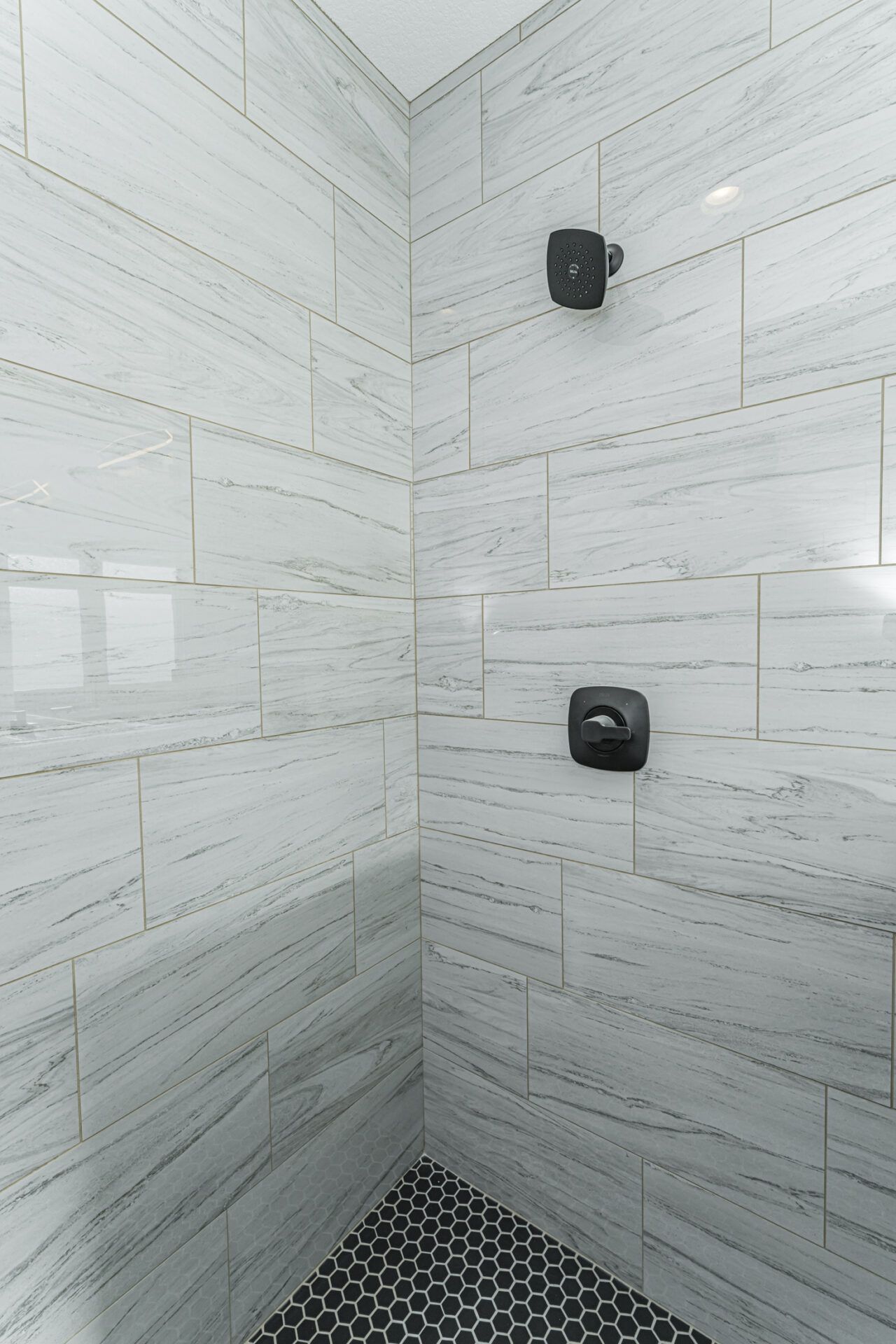 Shower with white marble-look tile walls and black hexagon tile floor; black shower fixtures.