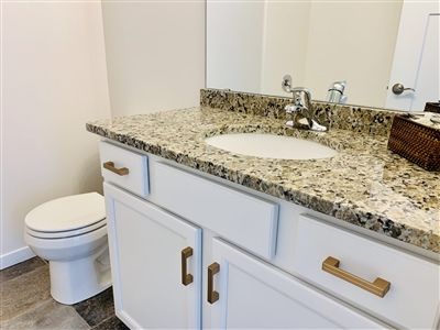 Bathroom with white vanity, granite countertop, oval sink, toilet, and mirror.