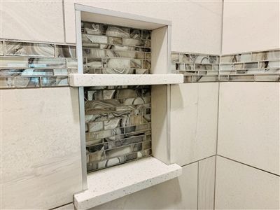 Built-in shower niche with stone-like tile backing and quartz shelves. Neutral colored tiles on walls.