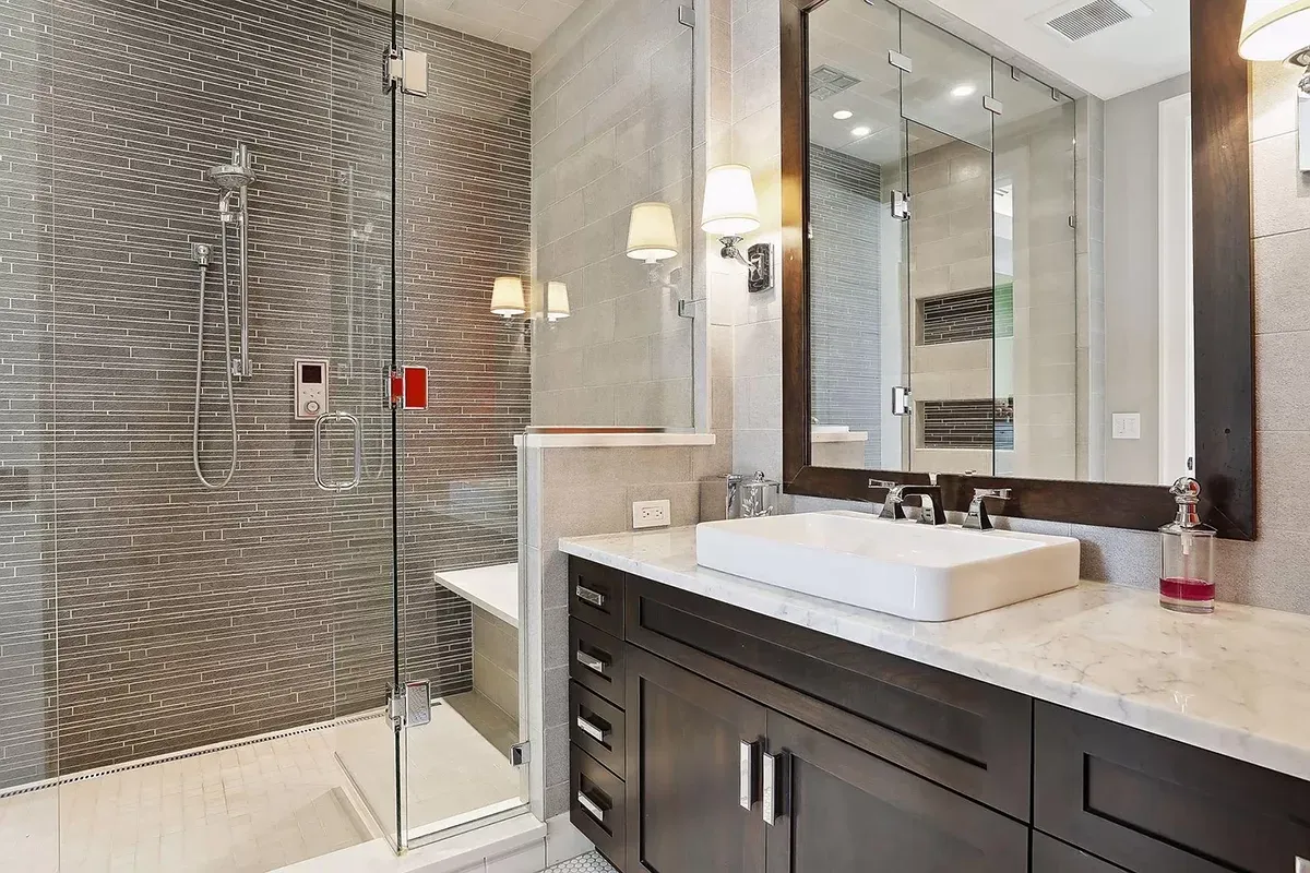 A bathroom with a sink , mirror and walk in shower.