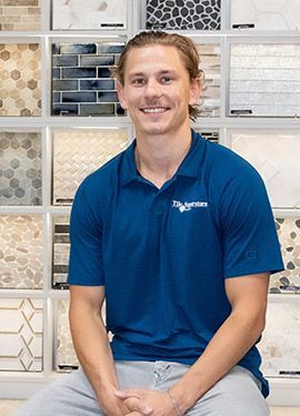 A man in a blue shirt is sitting in front of a wall of tiles.