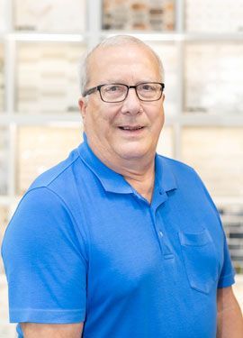 A man wearing glasses and a blue shirt is smiling for the camera.