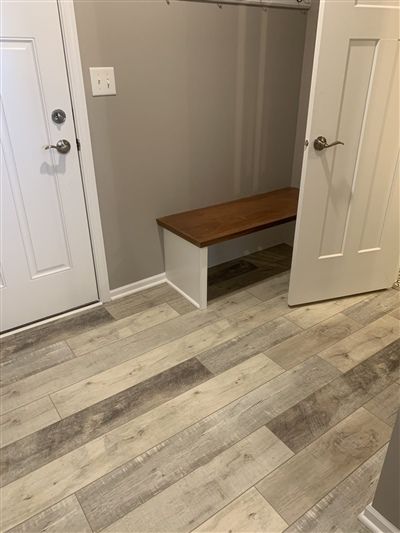 Small entryway with a wooden bench, two white doors, and light wood-look flooring.