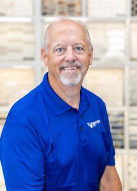 A man with a beard is wearing a blue shirt and smiling.