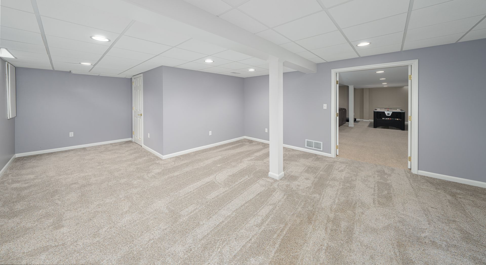 Empty basement room with light gray walls, white ceiling and support beam, and beige carpet.