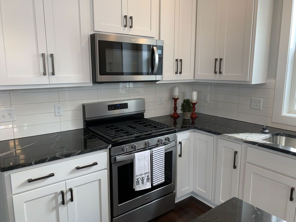 A kitchen with white cabinets , a stove , a microwave , and a sink.