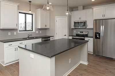 A kitchen with white cabinets , stainless steel appliances , granite counter tops and a large island.
