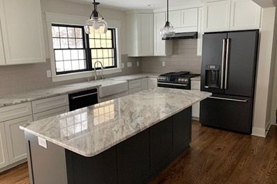 A kitchen with white cabinets , a black refrigerator , a stove , a sink , and a large island.