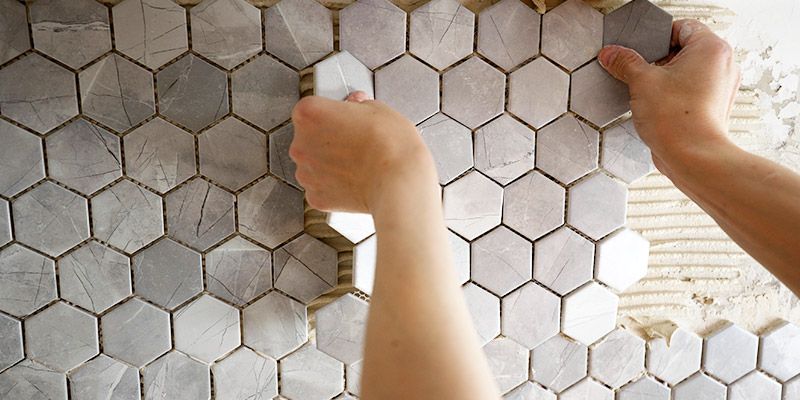 A person is laying hexagon tiles on a wall.