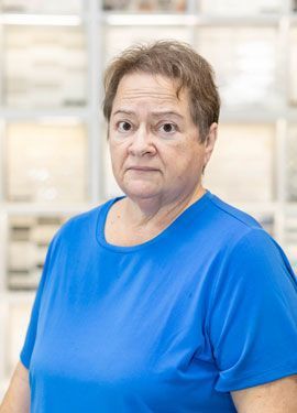 A woman in a blue shirt is standing in front of a shelf in a store.