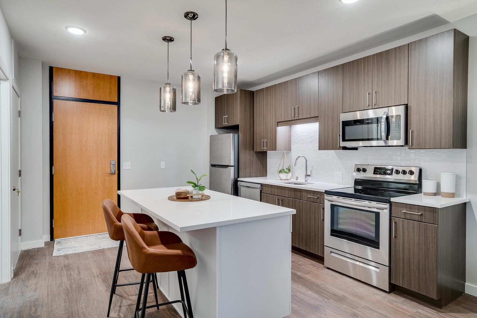 Modern kitchen with a large island, three pendant lights, wood-tone cabinetry, and stainless-steel appliances.