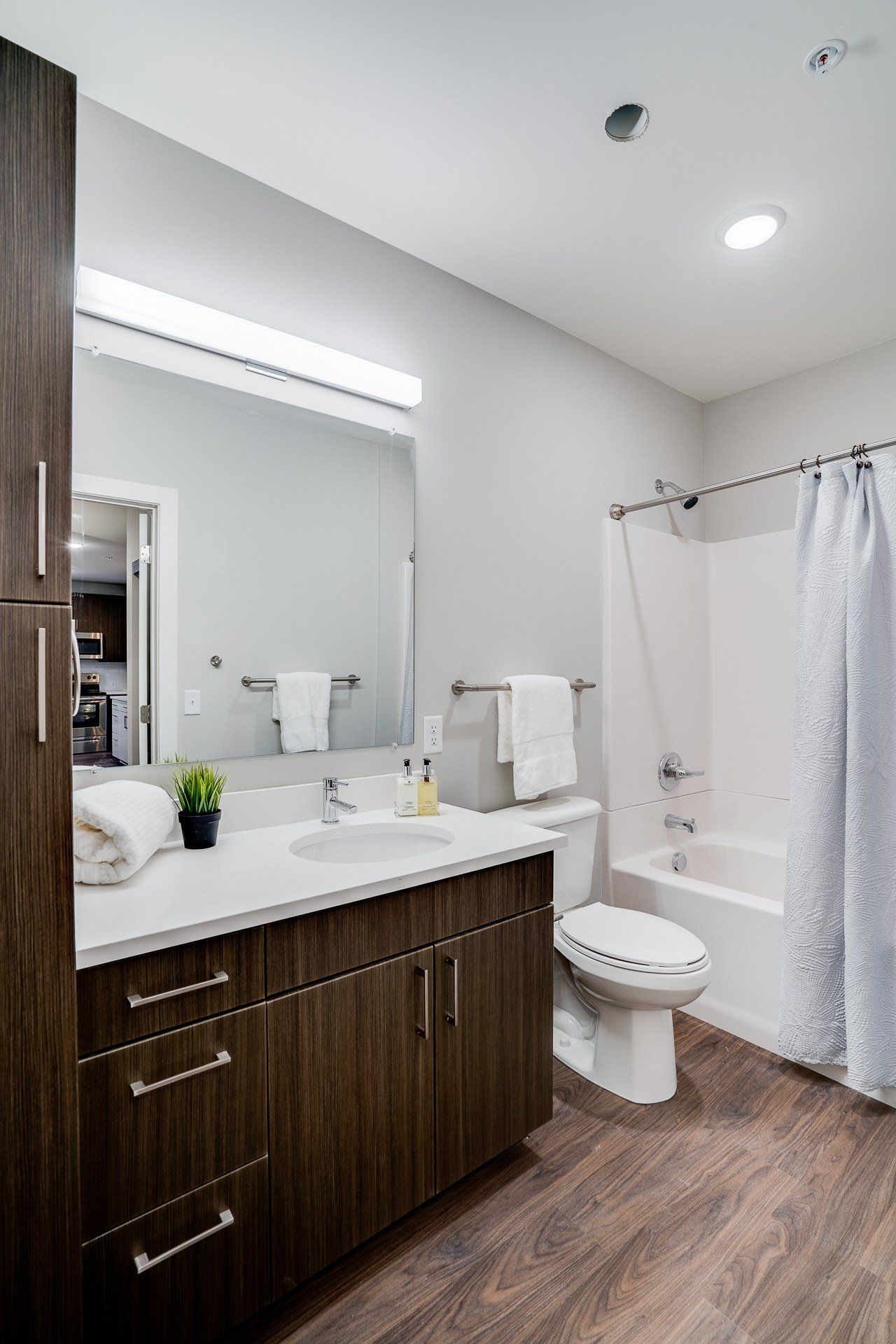 Bathroom in an apartment with a dark wood vanity, large mirror, towels, toilet, and tub/shower.