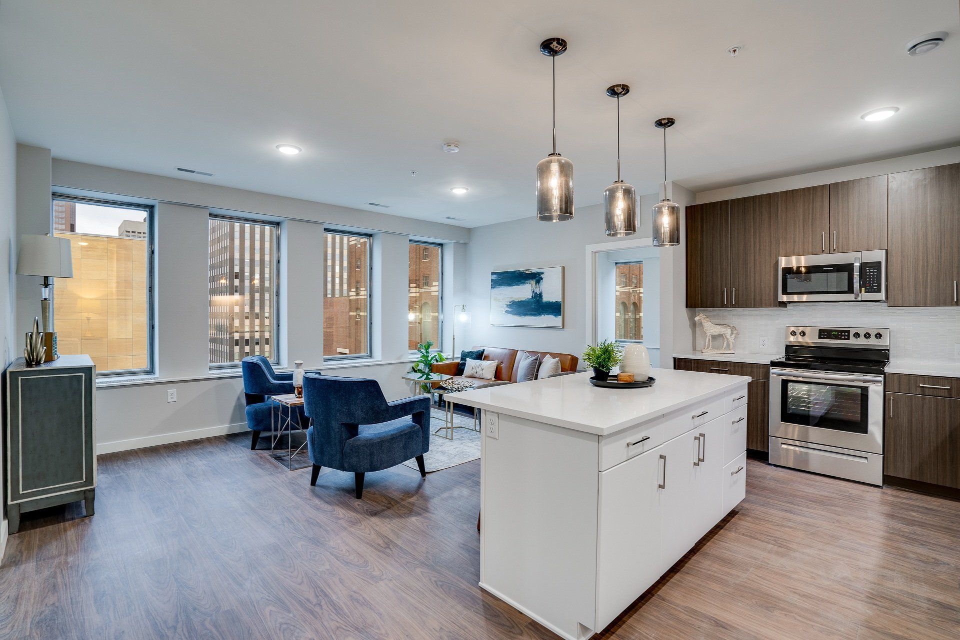 Open-concept kitchen and living area with white island, pendant lights, and wood floors.